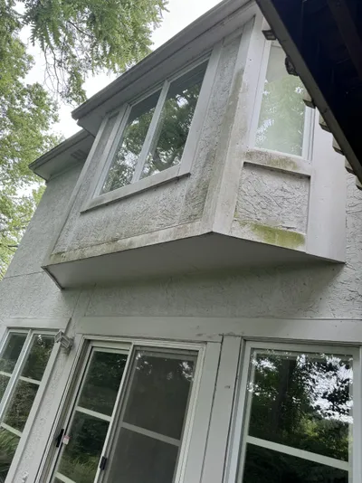 Pressure washing before — stucco siding with dirt and algae staining around bay windows.